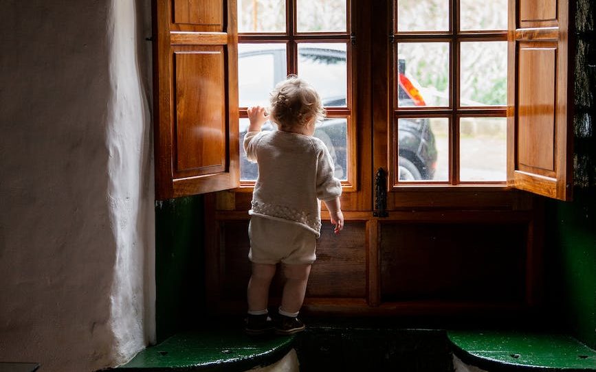 Baby looking out of the window of a holiday let. 